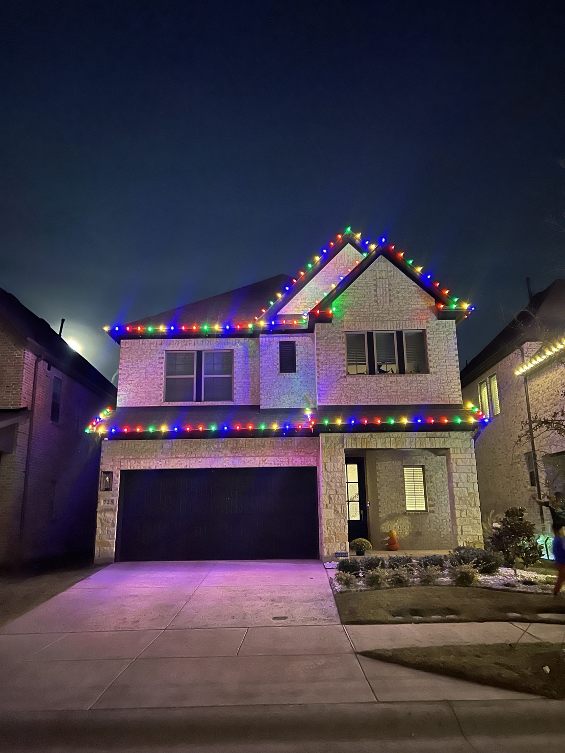 Two-story home with a multicolor seasonal Christmas roofline lighting display